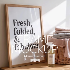May include: A wooden framed print with the words "Fresh. folded. & fabulous" in black. A spray bottle of "Lemon Linen" scent sits on a wooden surface next to a wicker basket with folded linens. The image is a mockup.