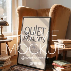 May include: A framed art print with the words "QUIET MOMENTS" and a floral illustration. The black framed print is propped against a mustard-colored armchair. Books and a small table lamp are also visible.