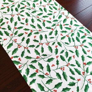 May include: White table runner with a repeating pattern of green holly leaves and red berries.