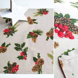 May include: A beige linen placemat with a repeating pattern of pine cones, holly leaves, and red berries. The placemat has a stitched edge.