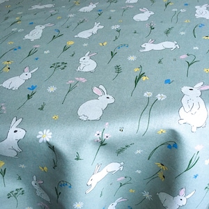 May include: A pale green fabric featuring a repeating pattern of white rabbits, flowers, and butterflies. The floral elements include daisies, bluebells, and yellow flowers. The rabbits are depicted in various poses.