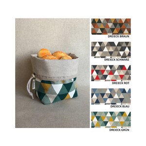 May include: A beige linen bread basket with a drawstring closure. The basket is lined with a green, white, and yellow geometric pattern of triangles. The basket is filled with bread rolls.