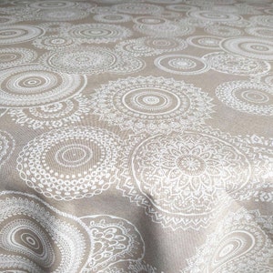 Pode incluir: Um tecido bege com um padrão de mandala branco. O tecido tem uma textura subtil e um aspeto suave e natural.