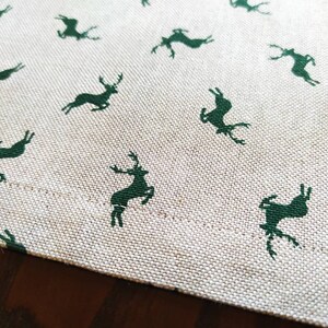 May include: A white tablecloth with a repeating pattern of dark green deer silhouettes.