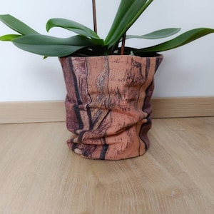 Könnte beinhalten: Eine Orchideenpflanze im Topf mit grünen Blättern in einem braunen und orangefarbenen Stofftopf mit Holzmaserung.