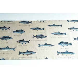May include: A beige fabric table runner with a repeating pattern of blue fish and their names. The fish include Atlantic Salmon, Lake Trout, Sea Bass, and more.