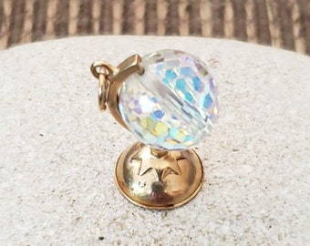 May include: A gold-toned globe charm with a clear iridescent glass globe. The globe is on a stand with a star design.