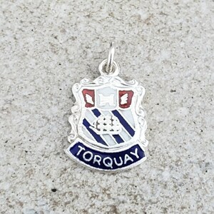 Peut inclure: Breloque en argent avec un écusson en émail bleu et blanc avec le mot "TORQUAY" en lettres blanches sur une bannière bleue.