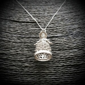 May include: A silver necklace with a pendant featuring a detailed, ornate design of a woman in a dress. The pendant is shaped like a bell.