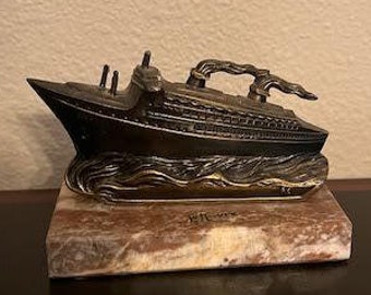 May include: A bronze figurine of a ship on a marble base. The ship has a detailed design and is set against a wave-like base.