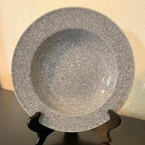 Puede incluir: Un cuenco de cerámica gris con un acabado moteado, exhibido en un soporte negro.