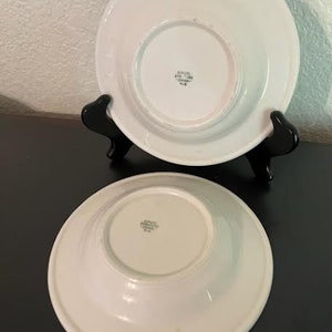 May include: Two white ceramic bowls with a raised rim. The bowls have a small, circular indentation in the center of the bottom. The bowls are marked with the text "Grace  England  China  514".