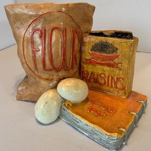 Fantastyczny, zabytkowy ceramiczny pojemnik na mąkę Cheryl Gadow z 1975 r., obok jajek, książki kucharskiej i rodzynek