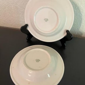May include: Two white ceramic bowls with a slightly raised rim. The bowls have a smooth, glossy finish and a small, centered indentation on the bottom. The bowls are marked with the text "JAPAN STONEWARE CHINA" in black.
