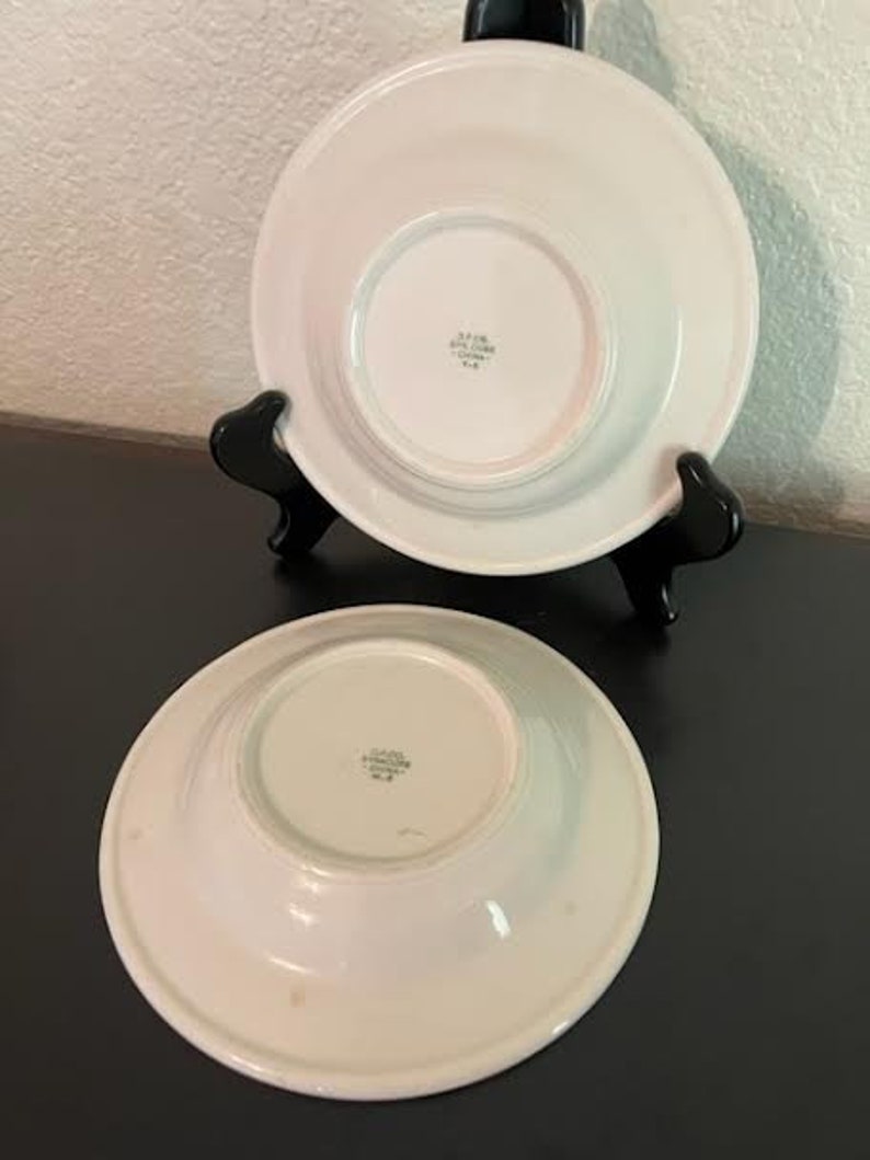 May include: Two white ceramic bowls with a slightly raised rim. The bowls have a smooth, glossy finish and a small, centered indentation on the bottom. The bowls are marked with the text "JAPAN STONEWARE CHINA" in black.