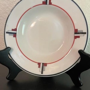 May include: A white ceramic soup bowl with a geometric design in red, black, and gray. The design features a series of rectangles and squares.