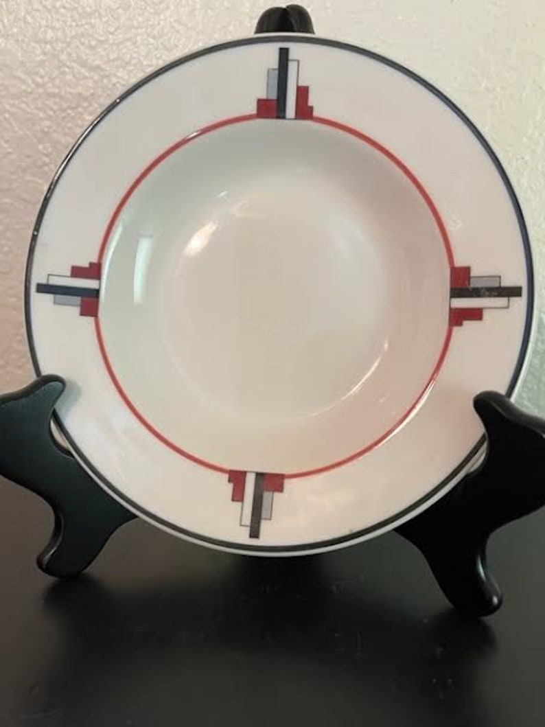 May include: A white ceramic soup bowl with a geometric design in red, black, and gray. The design features a series of rectangles and squares.
