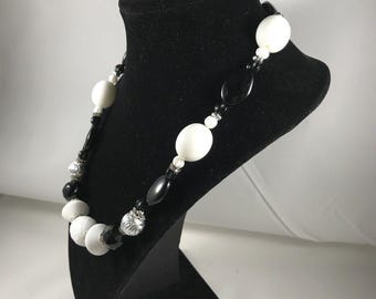May include: A black and white beaded necklace and bracelet set. The necklace features large white oval beads, black oval beads, and silver accents. The bracelet features smaller white and black beads.