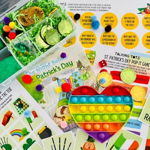 Op de afbeelding: Een regenboogvormig pop-it speelgoed in de vorm van een hart, een boek getiteld "The Night Before St. Patrick's Day" en een verscheidenheid aan St. Patrick's Day-thema-artikelen, waaronder groene munten, pompons en spelkaarten.