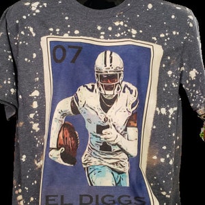 May include: A blue and white t-shirt with a bleach-splattered design. The shirt features a graphic of a football player in a blue jersey with the number "07" and the text "EL DIGGS".
