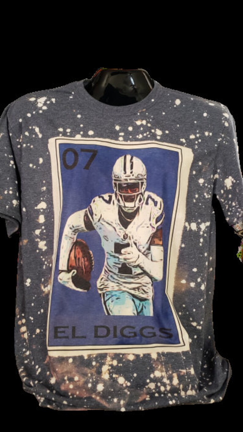 May include: A blue and white t-shirt with a bleach-splattered design. The shirt features a graphic of a football player in a blue jersey with the number "07" and the text "EL DIGGS".