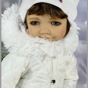 Puede incluir: Un abrigo de invierno blanco con capucha de piel sintética y diseño acolchado. El abrigo tiene un diseño de Mickey Mouse en la parte delantera y un gorro blanco con un diseño de Mickey Mouse en la parte superior.