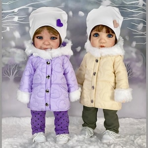 May include: Two dolls dressed in winter outfits. One doll wears a lavender quilted jacket with heart-shaped stitching, matching polka dot pants, and a white hat with a purple heart. The other doll wears a cream-colored quilted jacket, olive green pants, and a white hat with a pink heart. Both dolls wear white shoes.