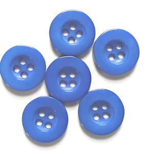 May include: A collection of six round, smooth, cornflower blue buttons, each featuring four central holes arranged in a square pattern. These circular fasteners have a slightly recessed center and a polished finish, presented in a cluster.