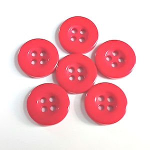 May include: A set of six round, bright red buttons arranged in a circular pattern. Each button features a smooth, glossy finish and four evenly spaced holes in the centre for threading, providing a consistent look across all pieces in the collection.