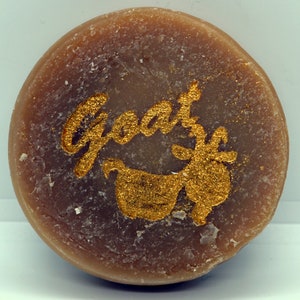 May include: A round, brown soap bar with the word "Goat" and a gold goat silhouette printed on it.
