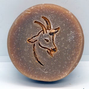 May include: A round, brown bar of soap with a gold-colored goat design embossed on the top.
