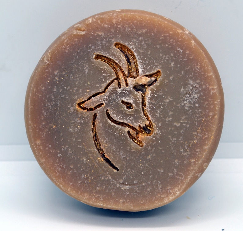 May include: A round, brown bar of soap with a gold-colored goat design embossed on the top.