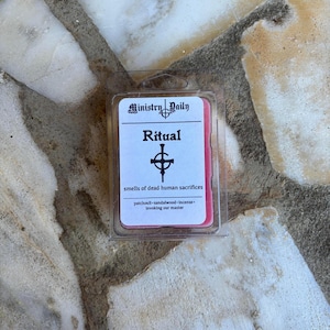 May include: A red wax melt in a clear plastic container with a white label that reads "Ministry Daily Ritual smells of dead human sacrifices patchouli-sandalwood-incense invoking our master"