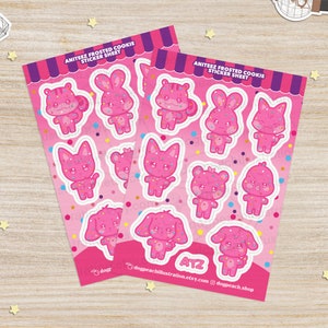 May include: Two pink sticker sheets featuring frosted cookie characters from the K-pop group Ateez. The characters are a bunny, a cat, a bear, a dog, and a squirrel. Each character has a pink frosting design and sprinkles. The sticker sheets are printed with the text "Ateez Frosted Cookie Sticker Sheet" and "ATZ".