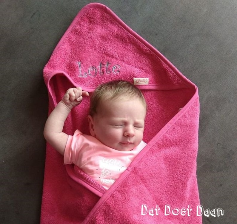 May include: A pink hooded towel with the name "Lotte" embroidered on it. A baby is wrapped in the towel and sleeping. The towel has the text "Dat Doet Daan" on the bottom.