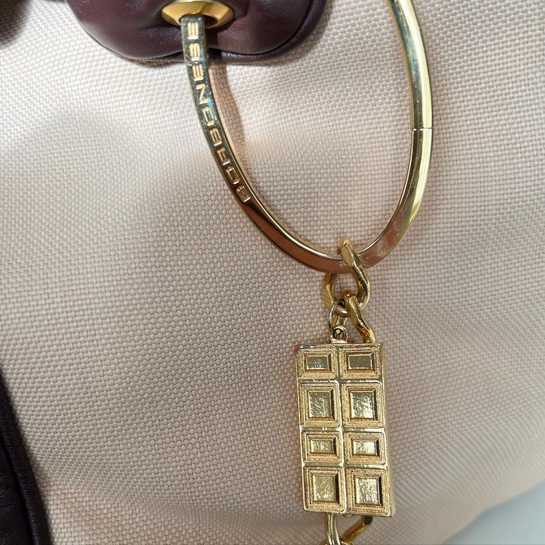May include: A gold-toned key chain with a rectangular charm featuring a grid pattern. The key chain is attached to a gold-toned ring with the word "EGOIST" engraved on it.