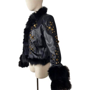 K&ouml;nnte beinhalten: Eine schwarze Lederjacke mit Pelzkragen und -&auml;rmeln. Die Jacke ist mit goldfarbenen Nieten verziert.