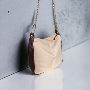 May include: A beige and brown shoulder bag with a gold chain strap. The bag has a zipper closure and a flap with a magnetic closure.