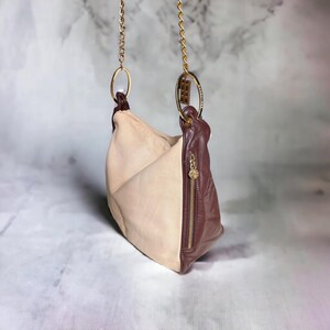 May include: A beige and brown leather handbag with a gold chain strap and a gold ring detail. The bag has a zipper closure and a flap.