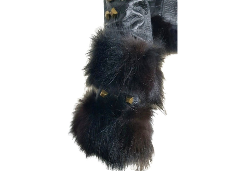 K&ouml;nnte beinhalten: Schwarze Lederjacke mit schwarzem Pelzbesatz an den &Auml;rmeln. Der Pelz ist dick und flauschig, und die Jacke hat goldfarbene Nieten an den Schultern.
