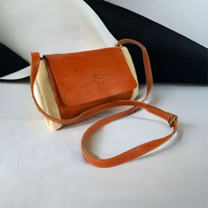 May include: A small, brown leather crossbody bag with a white fur lining and a brown leather strap. The bag has a small, embossed logo on the front.