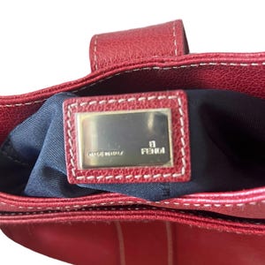 May include: Red leather handbag with white stitching. The interior is navy blue. A rectangular metal plate with the brand name "FENDI" is visible inside the bag. The words "MADE IN ITALY" are also on the plate.