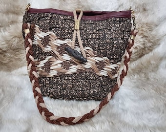 Può includere: Una borsa tote in tessuto marrone e beige con una parte superiore in pelle marrone e una tracolla in corda intrecciata. La borsa ha un design unico con un motivo intrecciato e un accento in pelle marrone.