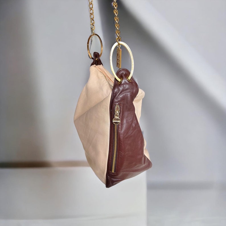 May include: A beige and brown leather handbag with a gold chain strap and two gold rings.