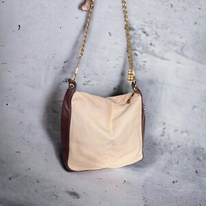 May include: A beige shoulder bag with a brown leather trim and a gold chain strap. The bag has a zipper closure and a small gold charm.