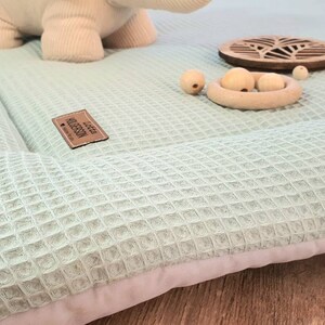 Könnte beinhalten: Eine hellgrüne Waffel-Spielmatte mit weißem Rand. Die Matte besteht aus weichem, bequemem Stoff und ist perfekt für Babys und Kleinkinder. Die Matte hat ein kleines Holzschild mit dem Text "Little Treasures" darauf.