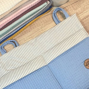 Può includere: Un organizzatore appeso blu chiaro con tessuto a righe bianche e una piccola etichetta marrone che dice "Lotta Holgersen".