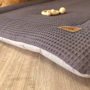 Könnte beinhalten: Eine graue Waffel-Spielmatte mit weißem Rand. Die Matte besteht aus weichem, bequemem Stoff und ist perfekt für Babys und Kleinkinder.