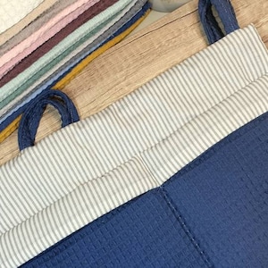 Può includere: Un organizzatore di stoccaggio appeso a strisce blu e bianche con una tasca e un'etichetta marrone che dice "Lotta Helseshop".