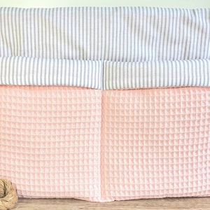 Può includere: Un organizzatore appeso rosa e bianco con due tasche. La tasca superiore è bianca con strisce grigie e la tasca inferiore è rosa con una texture a nido d'ape.